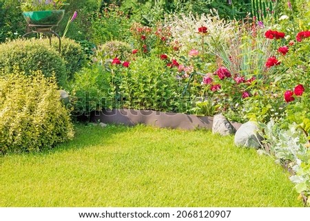 Part of a well-kept garden plot in the country house with a variety of blooming flowers and a green lawn.  Royalty-Free Stock Photo #2068120907