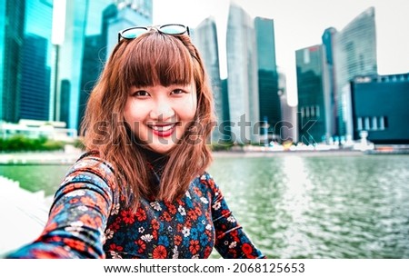 Young asian woman taking happy selfie traveling at Singapore skyline - Wanderlust life style concept with millenial girl having fun by urban city surrounds - Vivid bright filter with focus on face Royalty-Free Stock Photo #2068125653