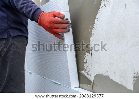 Construction worker installing styrofoam insulation sheets on house facade wall for thermal protection. Royalty-Free Stock Photo #2068129577
