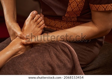 Experienced masseuse giving her client relaxing Thai foot massage