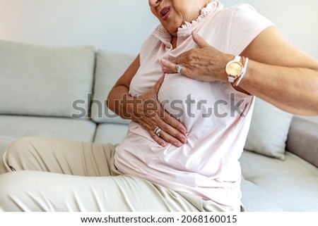 Senior woman hand checking lumps on her breast for signs of breast cancer on gray background. Healthcare concept. Caucasian woman palpating her breast by herself that she concern about breast cancer.