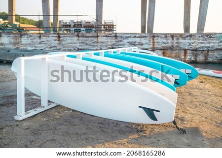 Group of blue SUP stand up paddle boards on the beach sand for tourist rent. Surfing boards on stand during summer season