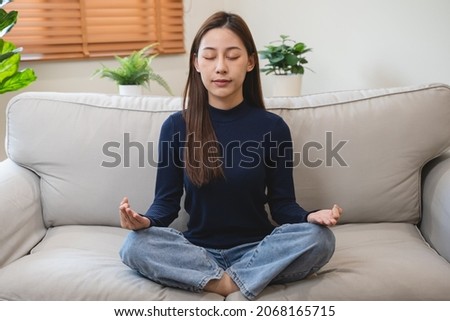 well being meditation. Asian women sit in the living room and practice mindfulness by focusing on breath concentrate.