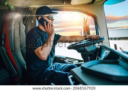 Portrait of handsome middle age man professional truck driver sitting and driving big truck. He is dangerously using his smart phone to talking with someone while driving. Royalty-Free Stock Photo #2068167920