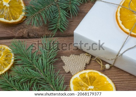 Christmas presents or gift box wrapped in kraft paper with decorations, pine cones, dry orange orange slices and fir branches on a rustic wooden background. Holiday concept