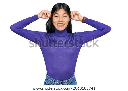 Beautiful young asian woman wearing casual clothes smiling pulling ears with fingers, funny gesture. audition problem 