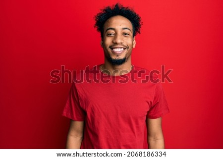 Young african american man with beard wearing casual red t shirt with a happy and cool smile on face. lucky person. 