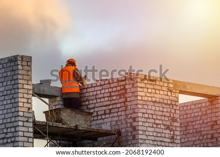 Bricklayer worker installing brick masonry on exterior wall. Professional construction worker laying bricks. Royalty-Free Stock Photo #2068192400