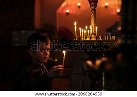 Little boy holding candle on dark background. A Child lights a candle in a chapel Royalty-Free Stock Photo #2068204550