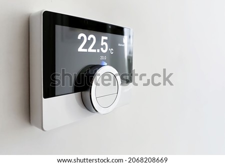 Screen of a smart digital thermostat with the external and target temperatures indicated. Rotary dial to control and adjust. Scheduling and programmable domestic heating. White wall and black frame Royalty-Free Stock Photo #2068208669