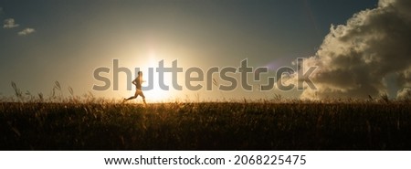 Male runner running in a field at sunset.  Royalty-Free Stock Photo #2068225475