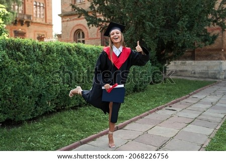 Beautiful female graduate celebrating graduation in university campus in robe with diploma.