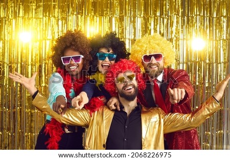Happy friends point fingers at camera inviting you to join 70s style fancy dress fun groovy disco party. Funny photobooth group portrait of excited young people at New Year Eve or birthday celebration Royalty-Free Stock Photo #2068226975