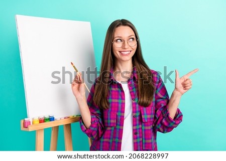 Portrait of trendy beautiful cheerful girl drawing new picture showing copy space isolated over bright teal color background