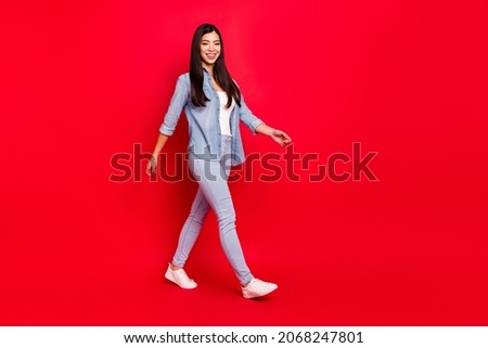 Full length body size view of attractive cheerful girl walking isolated over bright red color background