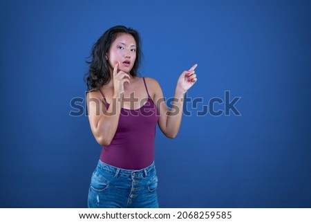 Beautiful young long-haired brunette chinese woman extending her hand to the side to show or indicate something.