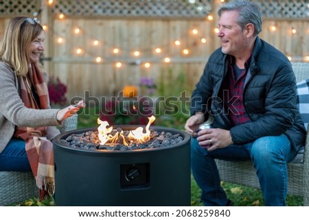 Happy middle age couple sitting by a backyard fire pit in fall Royalty-Free Stock Photo #2068259840