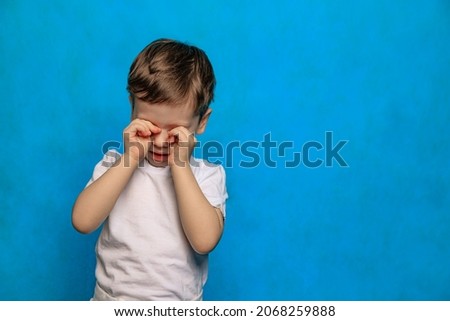 A boy on a blue background rubs his eyes . Eye health. Eye diseases. A crying baby. Fatigue of children. Psychology. Copy Space Royalty-Free Stock Photo #2068259888