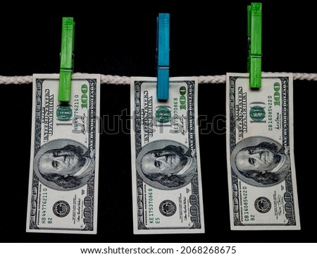 American hundred dollar bills hang on a rope with clothespins against a black background. Dirty money. Money laundering concept. 