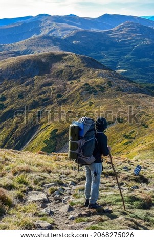 Hiker with a big backpack on a trail on a mountain ridge, back view
