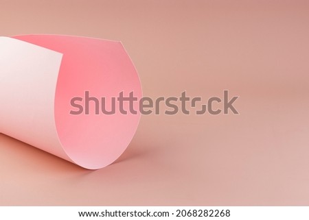 A sheet of pink paper rolled into a tube on a light background. Graphic concept