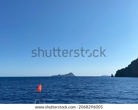 The waving Turkish flag on a calm sea background with a boat and blue sky.