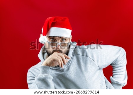 a bearded man in a red Santa Claus hat on a Christmas red background leaned his hand on his beard and thought
