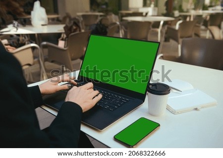 Close-up of female hands typing on laptop keyboard with green chroma key screen for ads. Mobile phone with green screen and copy space. Business, freelance, copywriting, online remote work concept