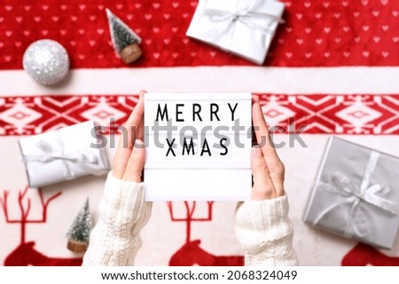 Close-up of lightbox with text merry christmas in hands and background with christmas gifts, miniature trees. Top view