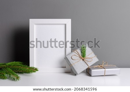 Photo or artwork frame mockup with christmas gift boxes and green fir tree branch over grey wall interior