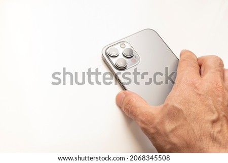 a hand holding a modern mobile phone from behind, with three cameras on a white background, copy space, cell, horizontal
