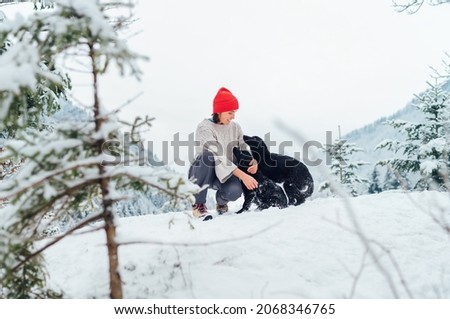 A young woman in warm knitted clothes walking her 2 dogs in a picturesque snowy mountain outdoor. Female smiling and playing with pets. Human and pets winter concept image