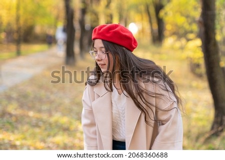 Girl in the red beret walking at the autumn park and looking down. Happy people