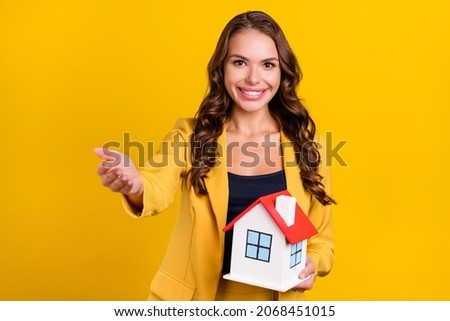 Photo of shiny beautiful young lady wear suit jacket inviting you holding arms hands small house smiling isolated yellow color background