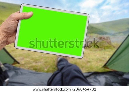 Male hiker hand showing tablet with blank green desktop screen with mountains on the background