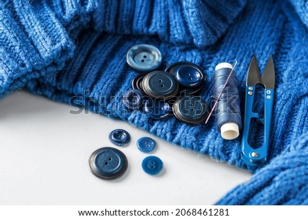 Blue Buttons and a spool of thread with a sewing needle on a blue knitted sweater. Sewing accessories. Copy space.