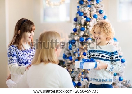 Child opening present at Christmas tree. Kids open gift on Xmas morning. Blue and white home decoration theme, Family celebrating winter holidays. Parents and children exchange presents.