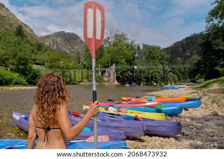 Horizontal view of unrecognizable woman with kayak on the river. Back view of woman in swimwear practicing canoeing in summer. Holidays and travel watersports concept. Royalty-Free Stock Photo #2068473932