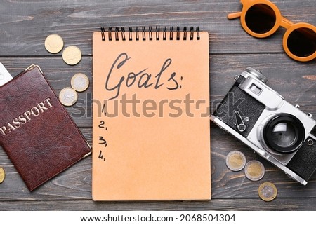 Notebook with empty to do list, passport, coins and photo camera on wooden background. New year goals