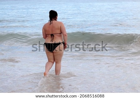 Overweight woman in black swimsuit going to swim in a sea water. Vacation on a beach, overeating and weight loss concept