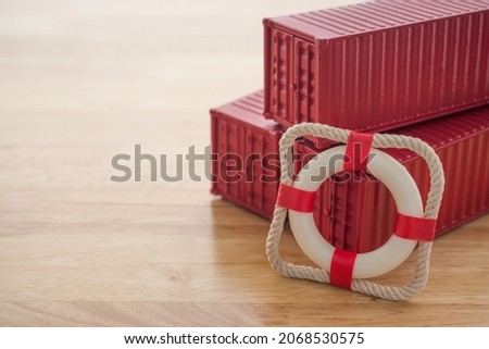 Lifebuoy with red containers on wooden table background with copy space. Marine cargo shipment or freight insurance in global shipping and logistic industry. Insurance is risk management control. Royalty-Free Stock Photo #2068530575