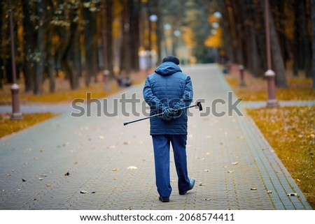 Elderly man walking with walking cane in hand behind his back. Old man with cane enjoying walk in autumn city park. Senior man walk alone. Royalty-Free Stock Photo #2068574411