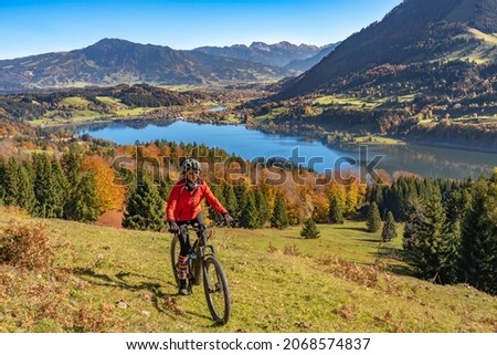 nice  woman with electric mountain bike enjoying the view over lake  Alpsee in atumnal atmosphere  in the Allgaeu alps above  Immenstadt, Bavarian Alps, Germany