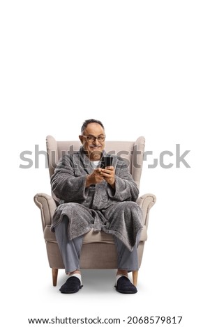 Mature man in a bathrobe sitting in an armchair and using a smartphone isolated on white background Royalty-Free Stock Photo #2068579817