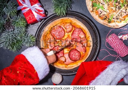 Christmas decorated background with pepperoni and mushrooms pizza,with Santa hands take pizza slice.  Delivery, restaurant Xmas Lunch party menu, Santa delivers pizza for Christmas, black table above