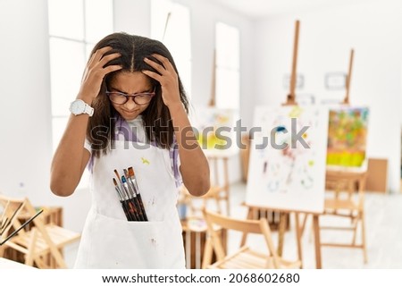 Young african american girl painting at art studio suffering from headache desperate and stressed because pain and migraine. hands on head. 
