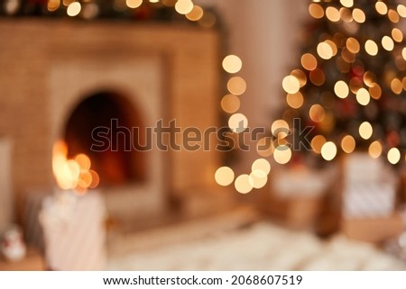 Blurred image of living room with fireplace and Christmas tree decorated with garland lights and many present boxes under xmas tree.