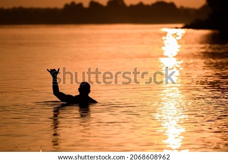 beautiful evening view of silhouette of a man in the water who shows the hand gesture shaka. Bright reflection of the sun in the water