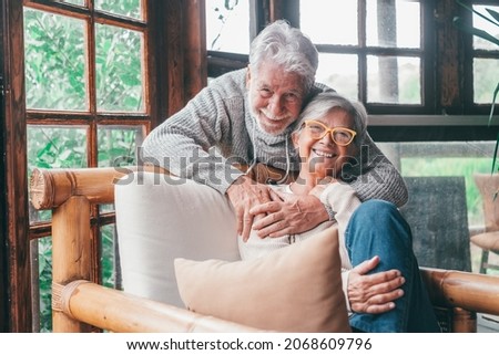 Portrait of cheerful senior couple embracing while sitting on sofa and smiling. Elderly happy couple relaxing and posing in front of camera sitting in living room. Royalty-Free Stock Photo #2068609796