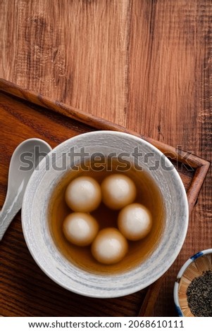 Top view of sesame big tangyuan (tang yuan, glutinous rice dumpling balls) with sweet syrup soup in a bowl on wooden table background for Winter solstice festival food. Royalty-Free Stock Photo #2068610111